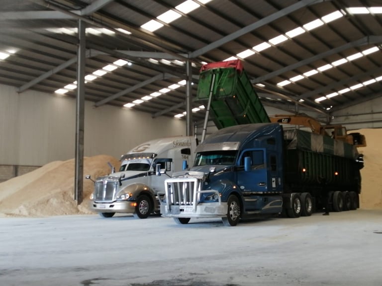 Camión de volteo descargando arena en instalación industrial con grandes pilas de material agregado