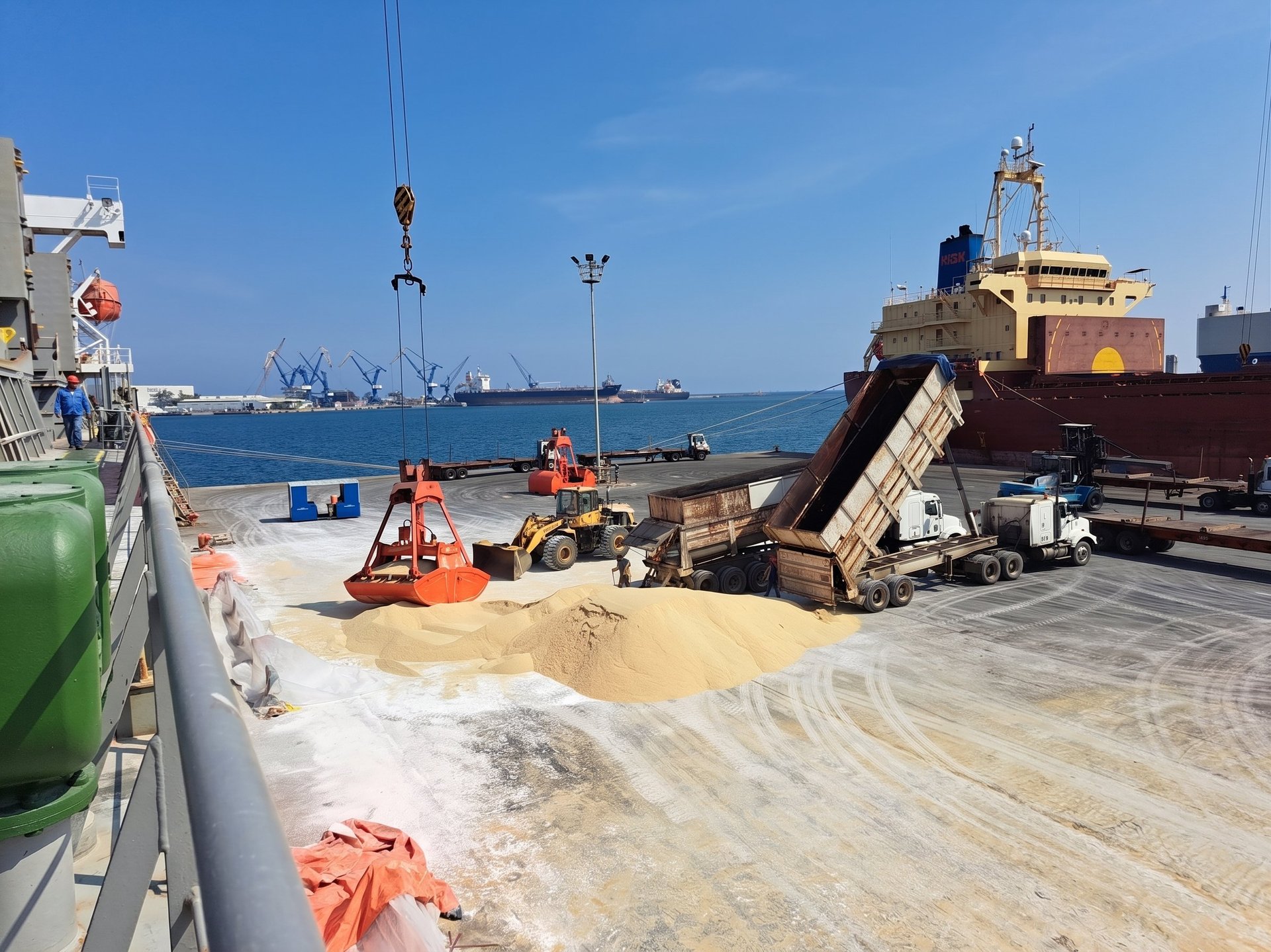 Cargo ship unloading sand and materials at port with construction equipment and ocean in background