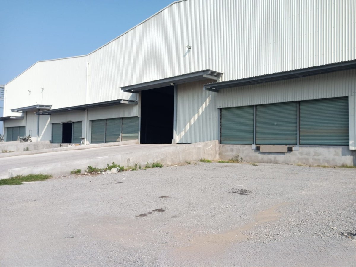Large industrial warehouse with corrugated metal exterior, loading dock entrance, and multiple windows under clear sky