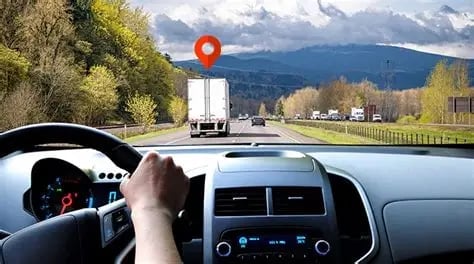 Drivers perspective from inside a car following a truck on a highway with mountains and green landscapes visible ahead