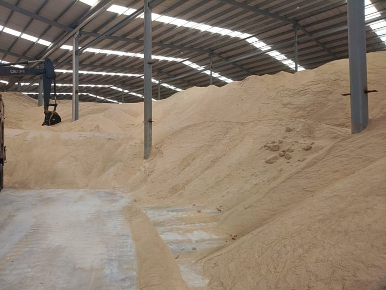 Large industrial warehouse with metal roof storing piles of sand or similar granular material