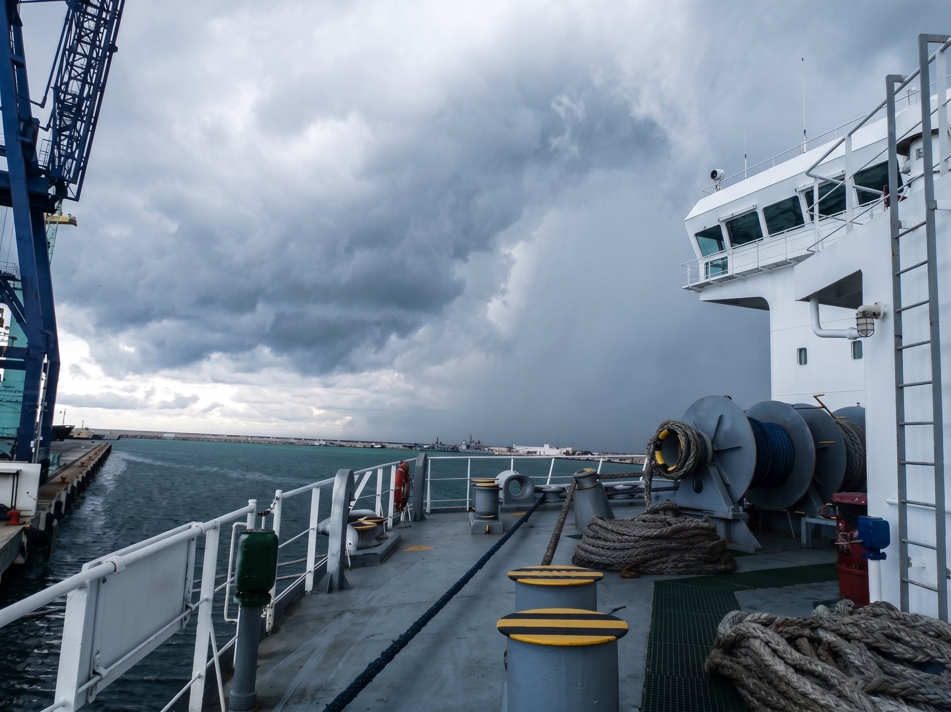 Ship deck with cargo equipment and winches overlooking choppy sea under stormy sky with dark clouds