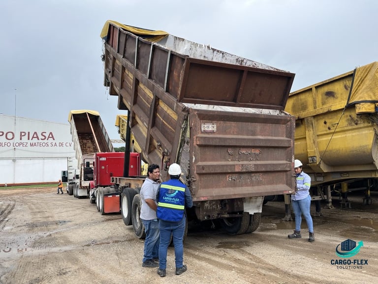 Two workers in safety vests observing a dump truck with raised bed at an industrial yard