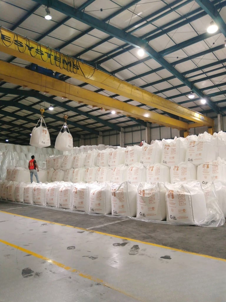 Almacén industrial con grúa pórtico amarilla y sacos blancos apilados, trabajador con chaleco naranja visible